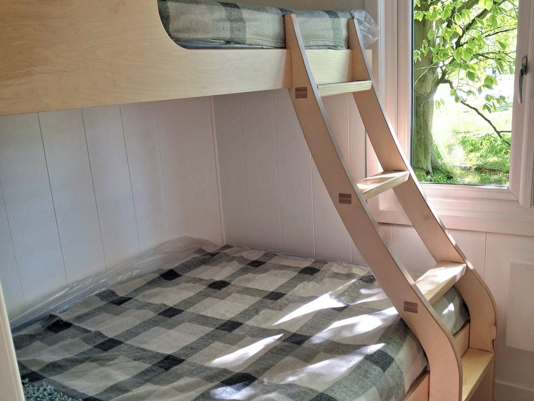 A bunk bed with a checkered bedspread and a window with a view of greenery.