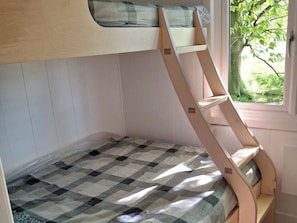 A bunk bed with a checkered bedspread and a window with a view of greenery.