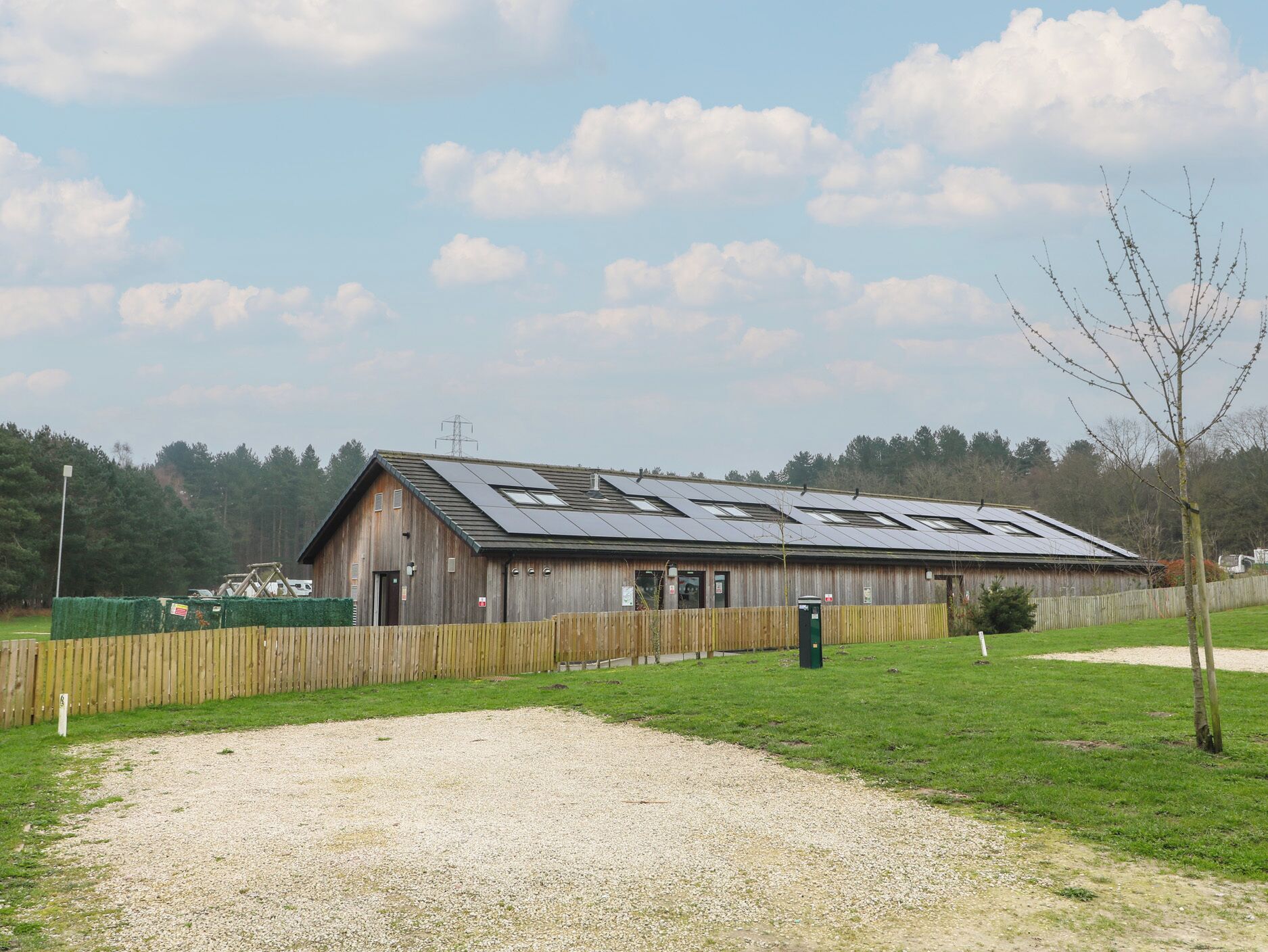 A wooden barn with solar panels on the roof, a gravel driveway, and a wooden fence.