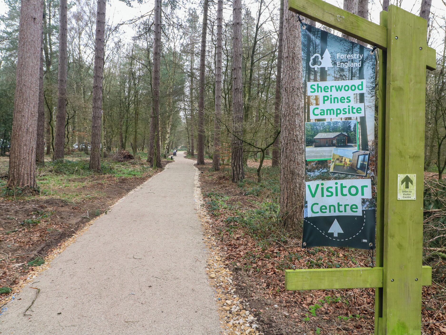 A forested path leading to a visitor center with a sign indicating Sherwood Pines Campsite and a 500m distance to the center.