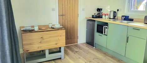 A compact kitchen with a wooden table, a microwave, a refrigerator, and a window with a view.
