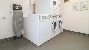 A laundry room with a stacked washer and dryer, an ironing board, and a wall-mounted control panel. - Sherwood Pines - Deluxe Pod 3 (Mansfield)