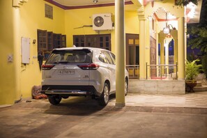 Ein weißer SUV parkt vor einem Gebäude mit gelben Wänden, einem Ventilator und einem Blumentopf.