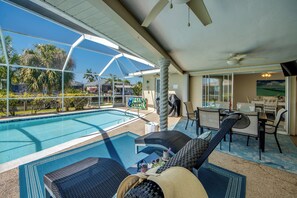 Un área junto a la piscina con sillones, una mesa de comedor y vistas a la piscina y palmeras.