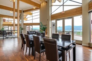 Un comedor amplio con una mesa larga y sillas, ventanas grandes con vistas, y una escalera que lleva a un nivel superior.