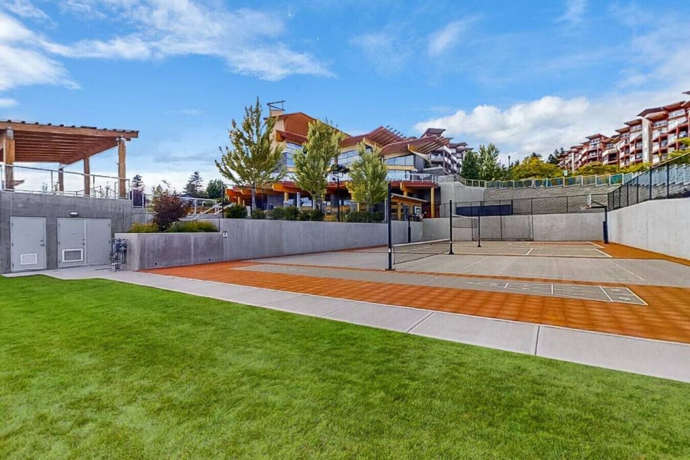 Una cancha de tenis con piso de madera, rodeada por un muro de concreto y una zona cubierta de césped.