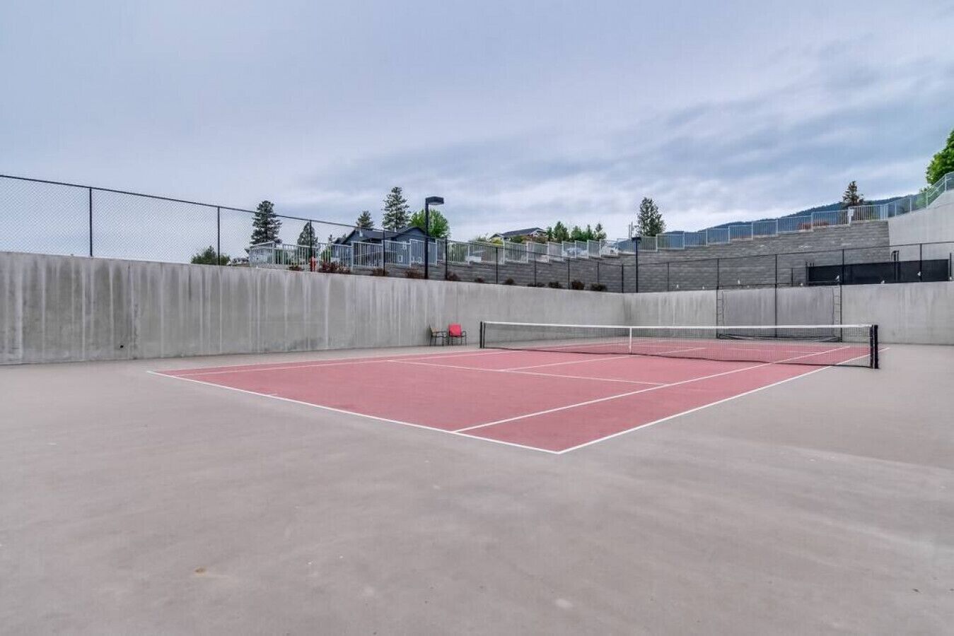 An outdoor tennis court with a net, surrounded by a concrete wall and a metal fence.