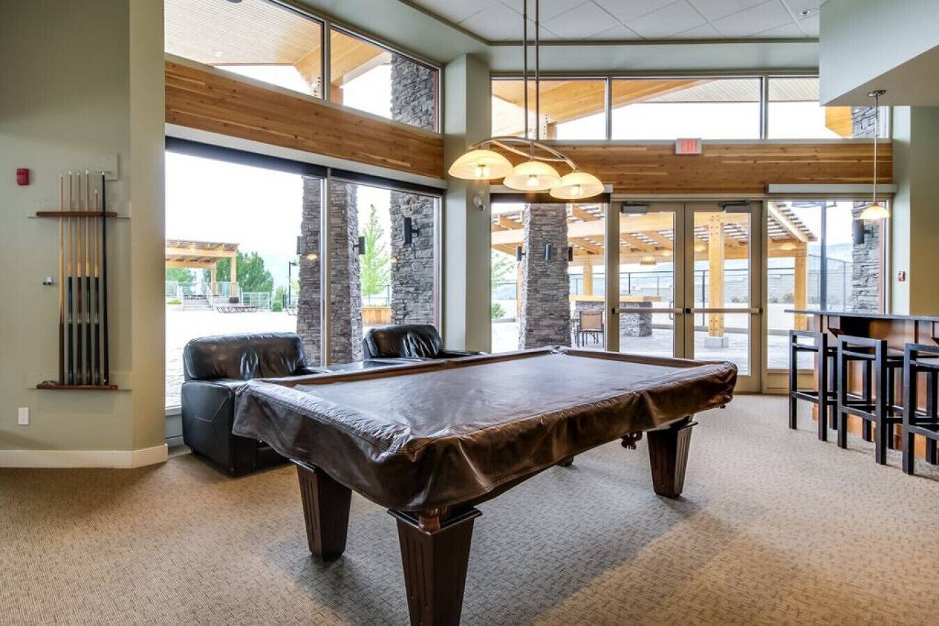 Una mesa de billar en una sala con ventanas amplias, una zona de bar y vistas al exterior.
