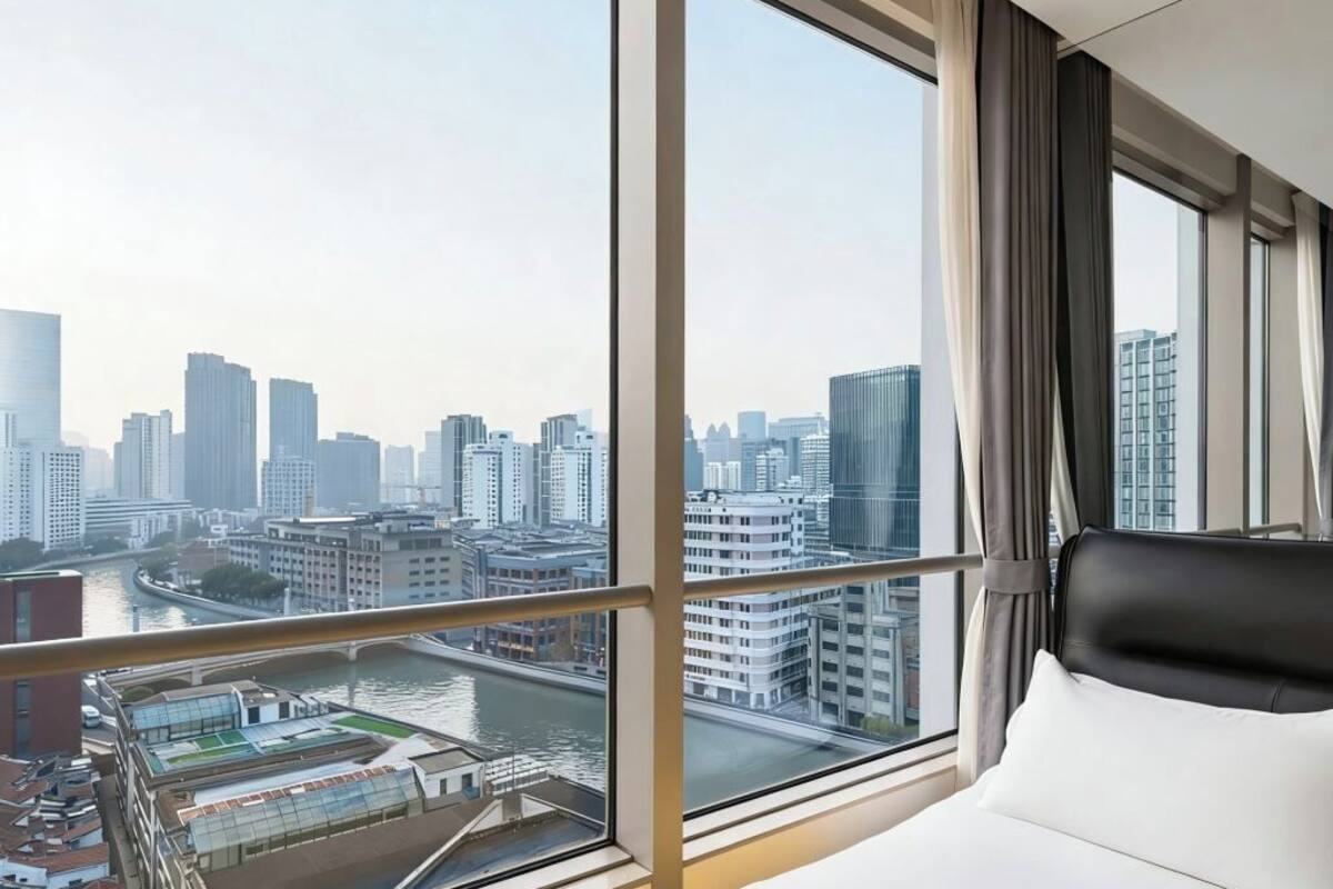 A hotel room with a large window offering a city view, a bed, and a view of a river.