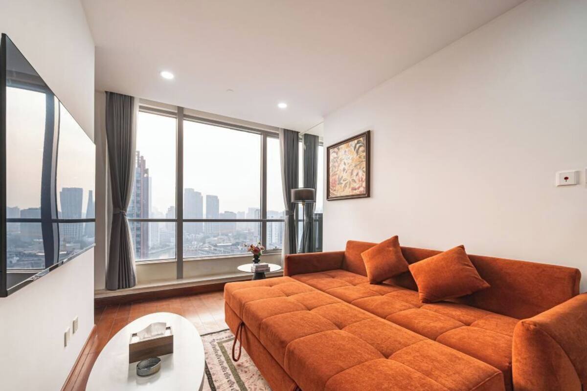 A modern living room with a large sofa, a small table, and a view of the cityscape through large windows.