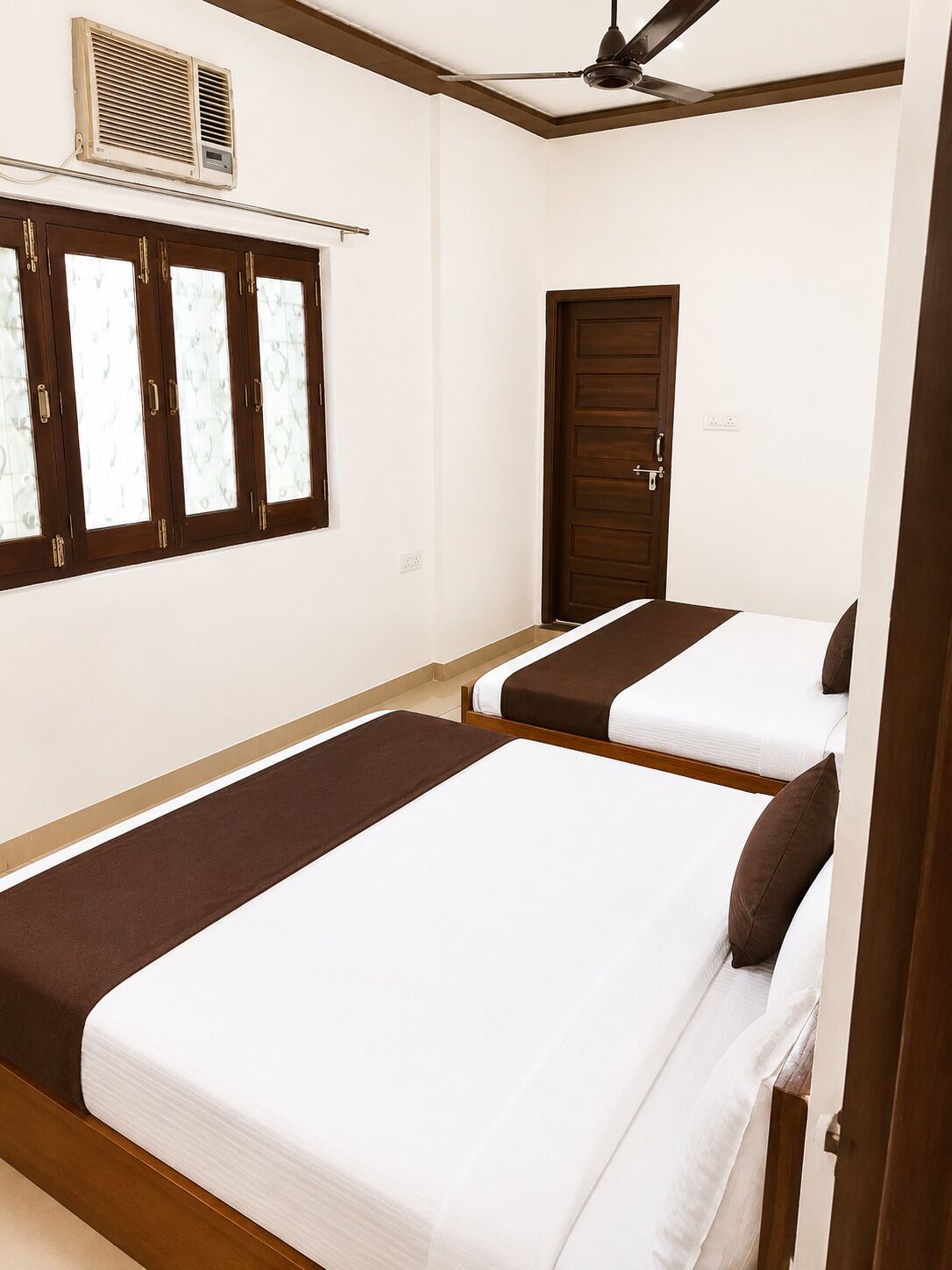 Een hotelkamer met twee bedden, een plafondventilator, een airconditioningsysteem en een deur.