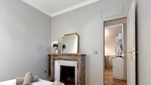 A bedroom with a bed, a fireplace, a mirror, and a door leading to a bathroom. -  Le Flandrin Céline 24 (Paris)