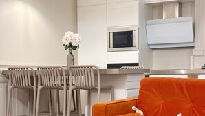 A modern kitchen with white cabinets, a microwave, and a dining area with chairs and a table. -  Le Flandrin Céline 24 (Paris)