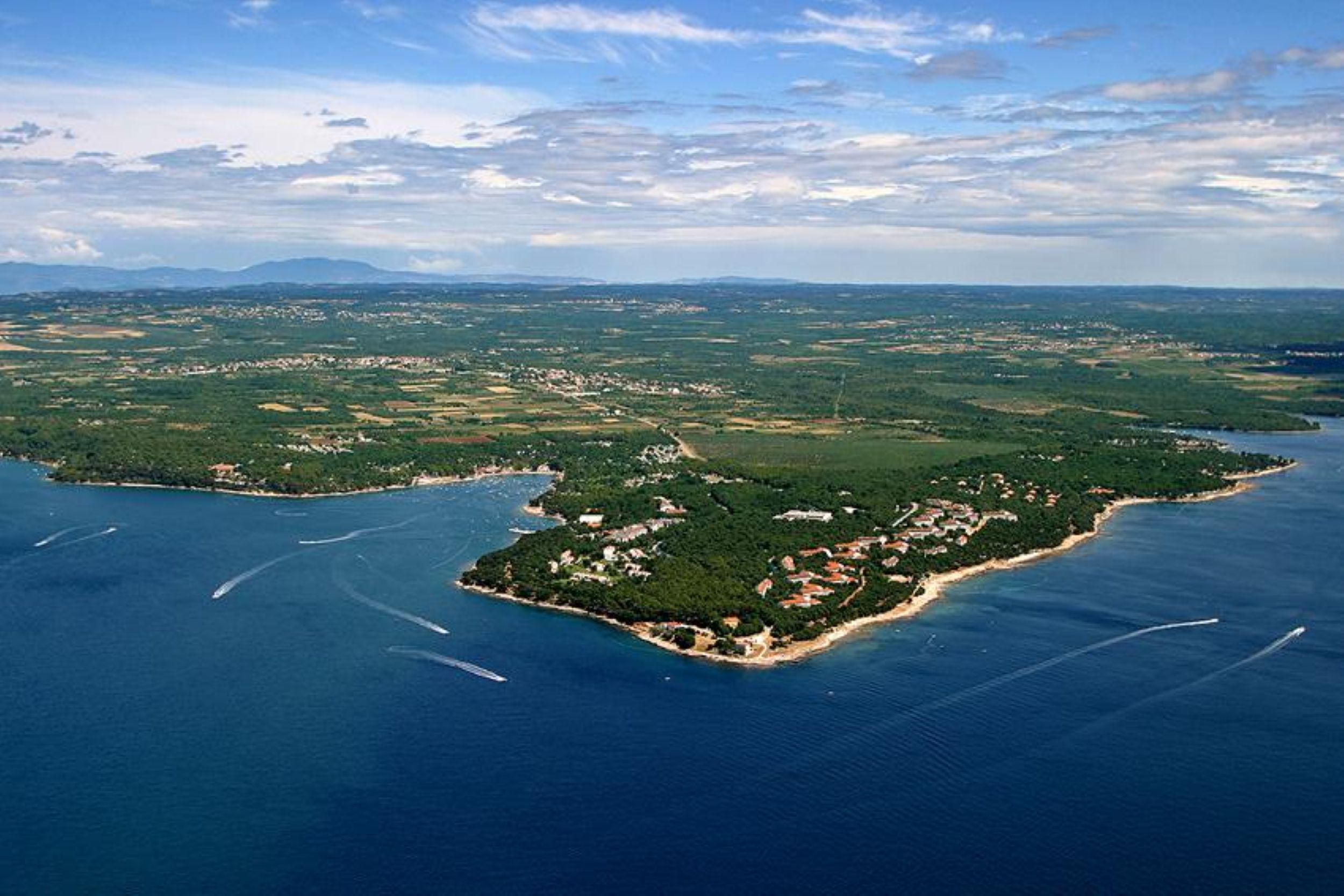 An aerial view of a coastal island with scattered buildings, surrounded by water and greenery.
