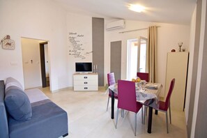 Uma sala de estar moderna com sofá, mesa de jantar com cadeiras, televisão em um móvel e uma parede com uma lista de nomes.