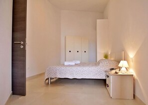A bedroom with a bed, a bedside table with a lamp, a wardrobe, and a door. - Modern poolside flat with game room acess (Tar)