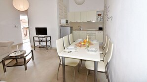 Une cuisine moderne avec des meubles blancs, une table à manger pour quatre personnes et un téléviseur posé sur un meuble.
