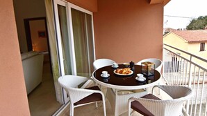 Un balcon avec une table ronde, des chaises en osier blanches et une table dressée avec des croissants et des tasses à café.