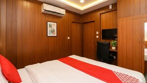 Una habitación de hotel con paneles de madera, una cama con cubrecama rojo y blanco, un televisor de pantalla plana en la pared y una pequeña planta en maceta.