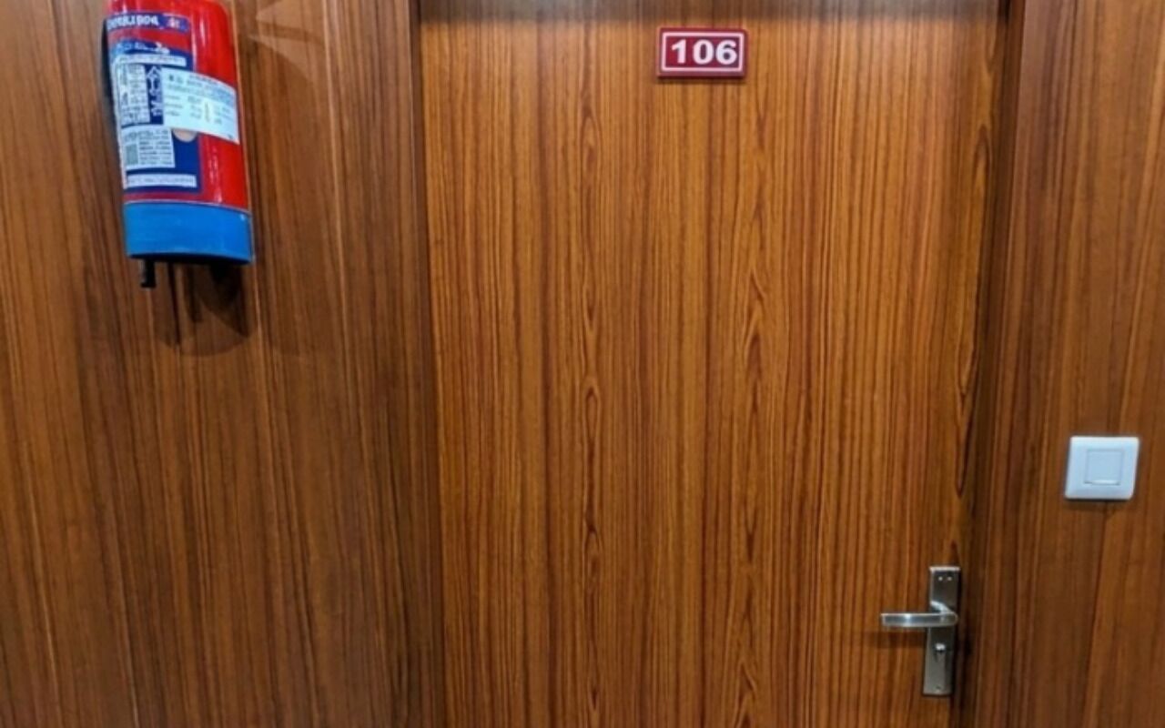 Een houten deur met een brandblusser aan de linker muur en een deurkenteken erboven.