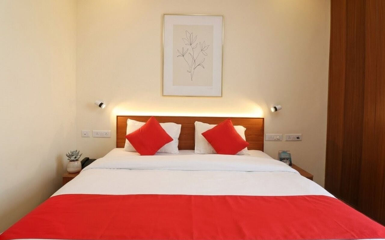 A neatly made bed with a red and white bedspread, two red pillows, and a framed artwork above the headboard.