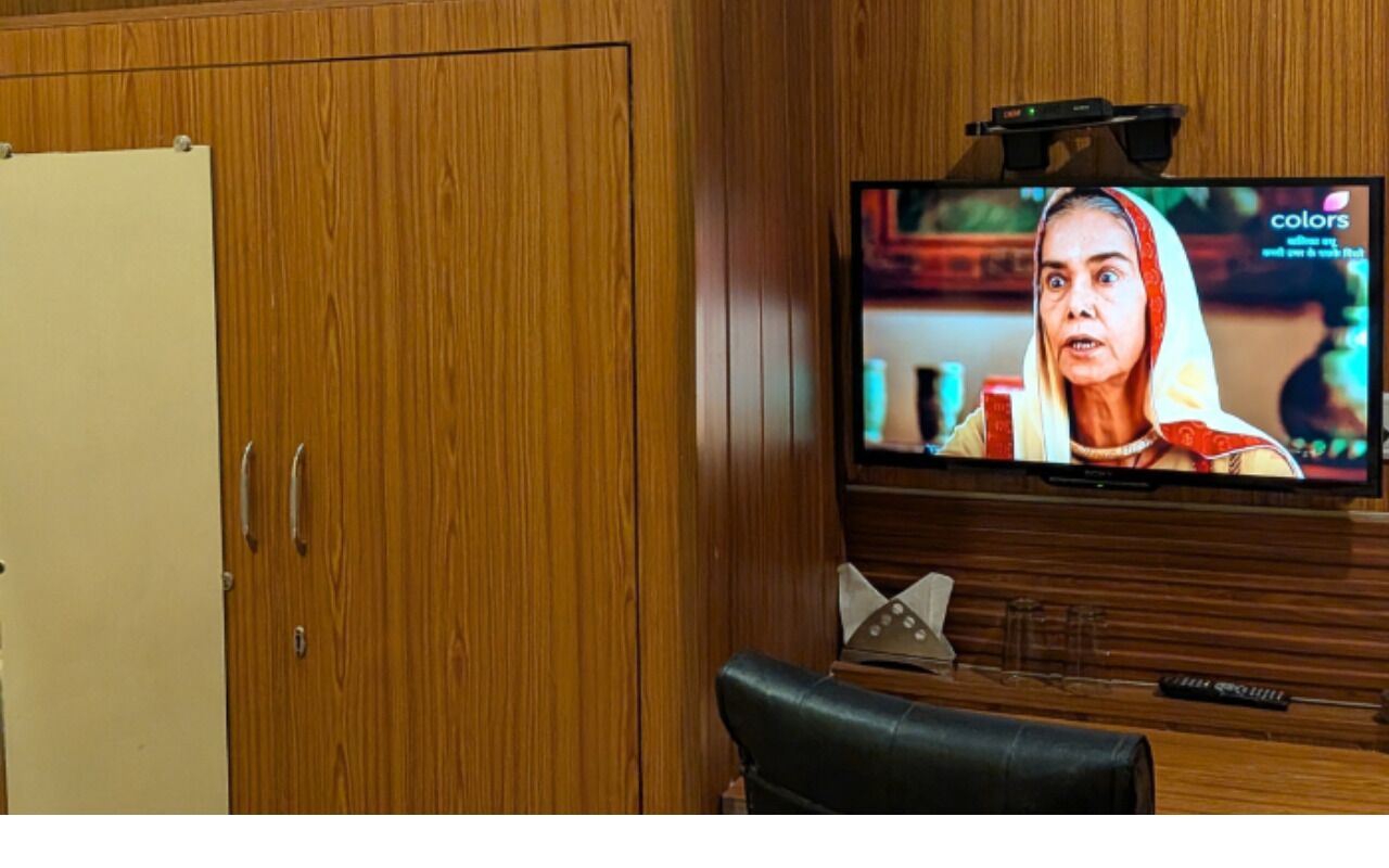 A television mounted on a wooden wall, a wooden cabinet, and a black leather chair.