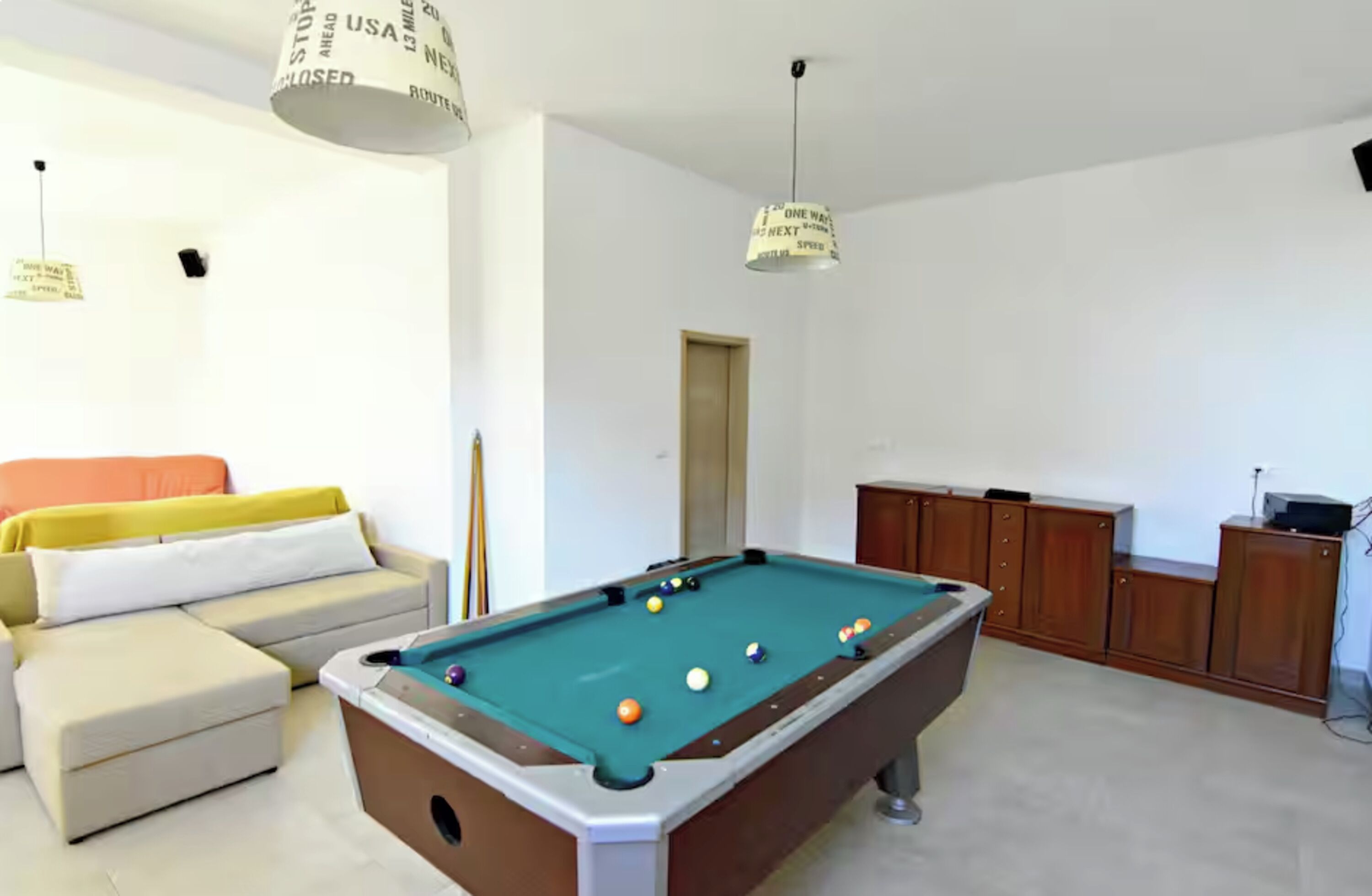 A pool table with balls, a sofa, and a cabinet in a room with white walls.