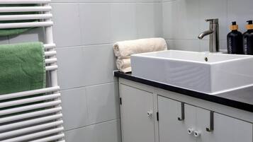 Ein Badezimmer mit weiß gefliester Wand, einem weißen Heizkörper, einem Waschbecken mit schwarzer Arbeitsplatte und einem Spiegel über dem Waschbecken.