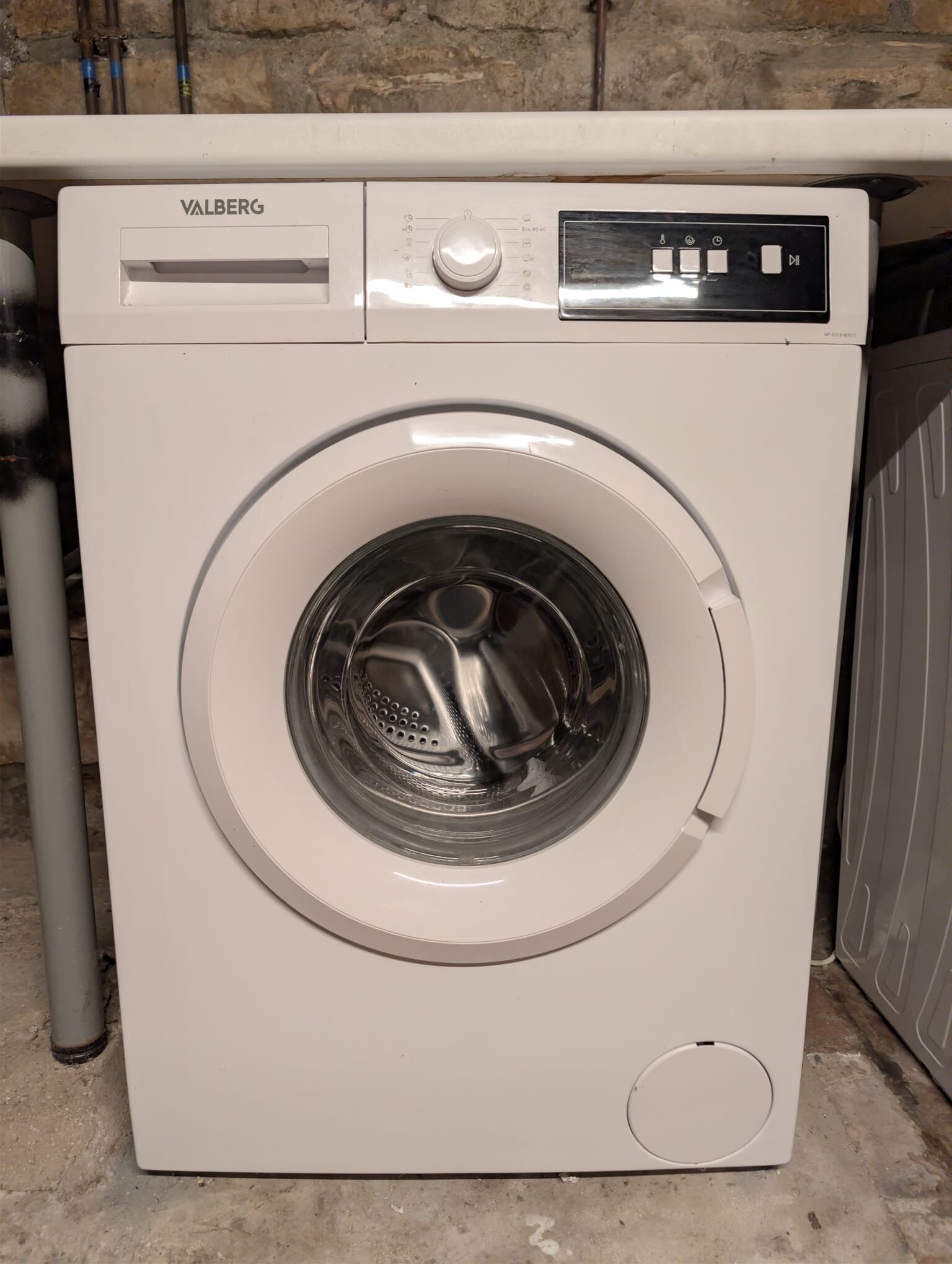 Un lave-linge Valberg blanc, doté d’un panneau de commande, d’une porte transparente et d’une petite ouverture circulaire située en bas.