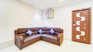 A corner living room with a brown leather sofa, a wooden door with geometric patterns, and a ceiling-mounted air conditioning unit. - Super Hotel O Aarapalayam (Madurai)