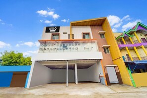 Un hôtel à plusieurs étages, avec une enseigne indiquant « HÔTEL » et un parking situé devant.