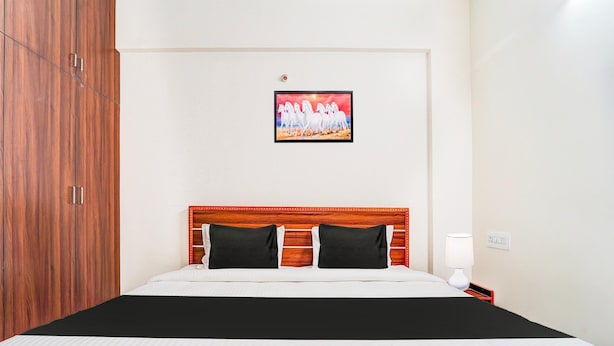 A hotel room with a wooden wardrobe, a bed with black and white bedding, a headboard with a red trim, and a framed picture on the wall. - Super Hotel O Aarapalayam (Madurai)