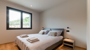 A modern bedroom with a large bed, a nightstand, a window with a view of greenery, and a built-in shelf. - Villa Aqua_Giuly Suite Apartment_Lake View & Pool (San Felice del Benaco)