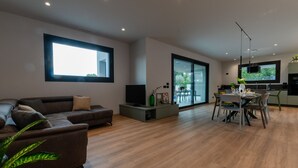 A modern living room with a sofa, TV, and dining area with chairs and a table. - Villa Aqua_Giuly Suite Apartment_Lake View & Pool (San Felice del Benaco)