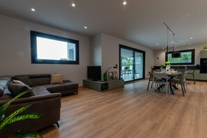 Una sala de estar moderna con sofá, televisor y comedor con sillas y mesa.