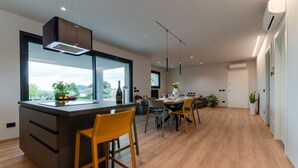 A modern kitchen with a large island, dining area with chairs, and a view of greenery outside. - Villa Aqua_Lydia Suite Apartment_Lake View & Pool (San Felice del Benaco)
