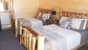 Un dormitorio de cabaña de madera con dos camas, una mesita de noche, una lámpara y un espejo.