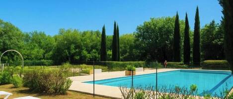 A rectangular swimming pool with a surrounding deck, surrounded by greenery and trees.