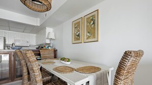 A dining area with wicker chairs, a white table, and two framed floral paintings on the wall. - Three Bedroom Two Bath Townhome Directly On The Bay (Ocean City)