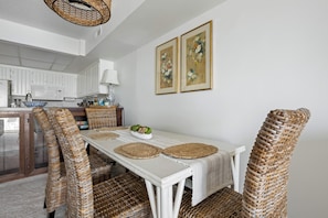 A dining area with wicker chairs, a white table, and two framed floral paintings on the wall. - Three Bedroom Two Bath Townhome Directly On The Bay (Ocean City)