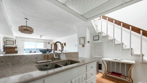 A kitchen with a sink, white cabinets, a marble countertop, a hanging light fixture, and a view to the outside. - Three Bedroom Two Bath Townhome Directly On The Bay (Ocean City)