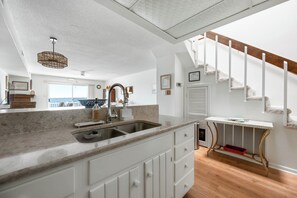 A kitchen with a sink, white cabinets, a marble countertop, a hanging light fixture, and a view to the outside. - Three Bedroom Two Bath Townhome Directly On The Bay (Ocean City)