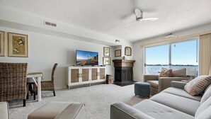 A living room with a television, fireplace, and large windows overlooking a body of water. - Three Bedroom Two Bath Townhome Directly On The Bay (Ocean City)