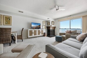 A living room with a television, fireplace, and large windows overlooking a body of water. - Three Bedroom Two Bath Townhome Directly On The Bay (Ocean City)