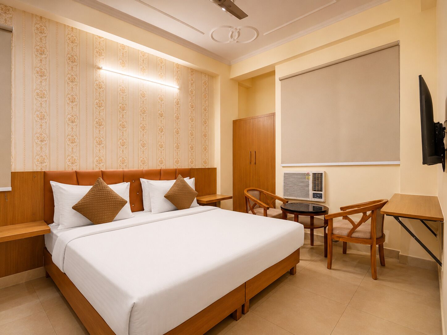 A hotel room with a large bed, a desk with a chair, a wardrobe, and a television.