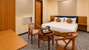 A hotel room with a bed, two chairs, a table, a bedside table with a phone, and an air conditioning unit. - SnapStayz (Noida)