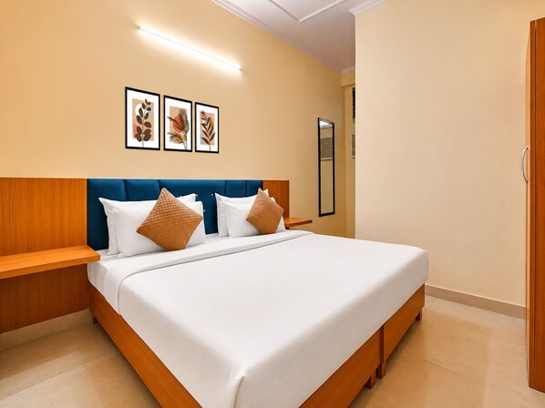 Habitación de hotel con una cama grande, cabecera de madera, ropa de cama blanca y un espejo adosado a la pared.