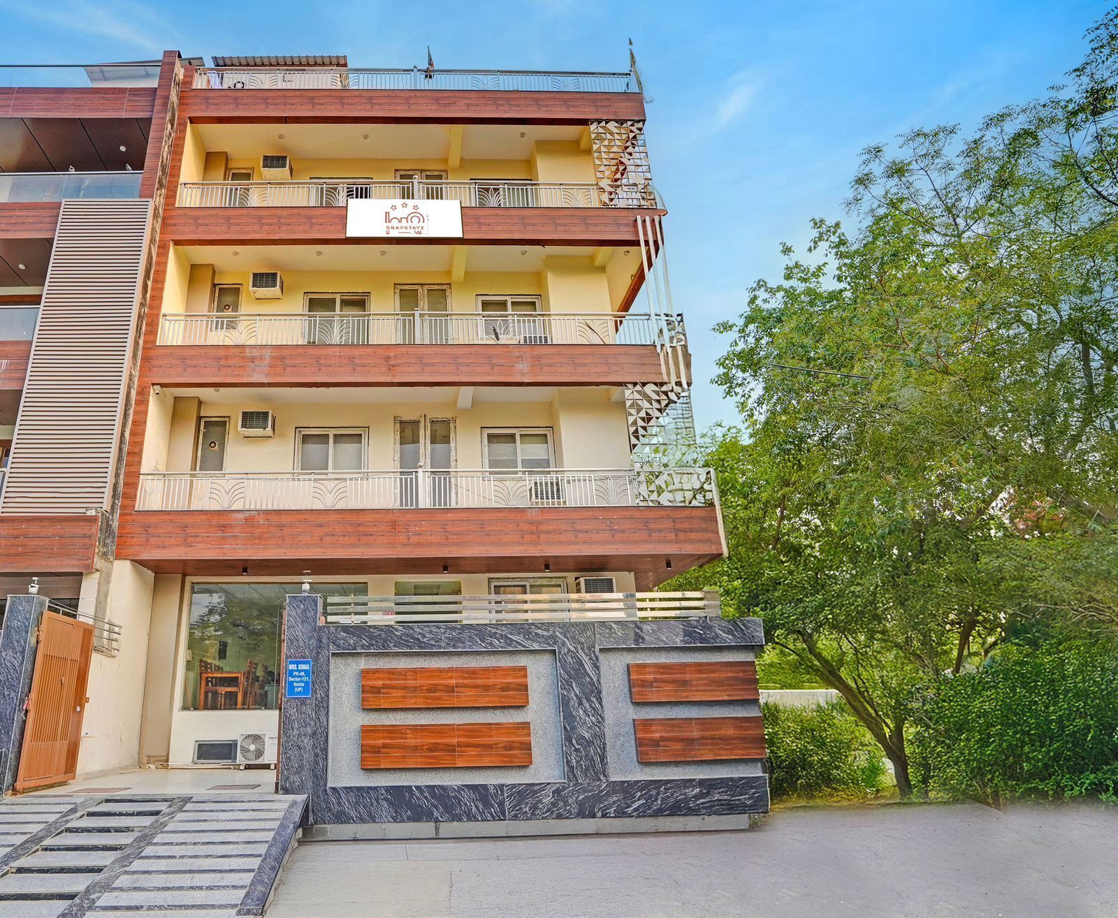 Un hotel de varios pisos con balcones, un cartel que indica 'Shapstaz' y una entrada con portón.