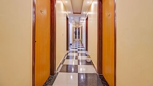 A hotel hallway with checkered flooring, wooden doors, and a ceiling with recessed lighting. - SnapStayz (Noida)