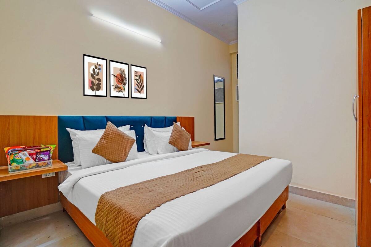 Quarto de hotel bem arrumado, com uma cama, mesa de cabeceira com lanches, espelho e obras de arte nas paredes.